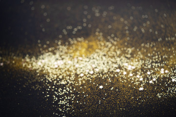 Beautiful Christmas light background. Abstract glitter bokeh and scattered sparkles in gold color, on black