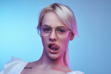 Closeup portrait of a passionate blonde girl wearing glasses poses with tongue sticking out looking...