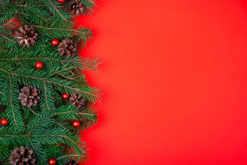 Christmas tree branches decorated with pine cones over red festive background. Flat lay.