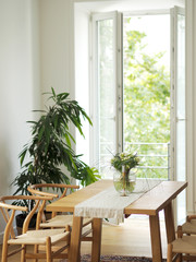 Fresh flowers in glass vase standing on a wooden table in white dining room interior with oriental carpet. Interior design in minimal style.