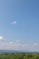 Obraz premium hilly landscape rich in tree vegetation with some houses and cloudy blue sky