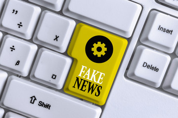 Conceptual hand writing showing Fake News. Concept meaning Giving information to showing that is not true by the media White pc keyboard with note paper above the white background