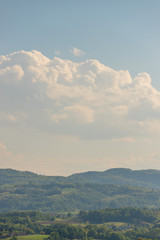 Fototapeta premium hilly landscape rich in tree vegetation with some houses and cloudy blue sky