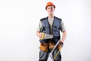 A builder with hacksaw in a helmet, smiling. On a light background.