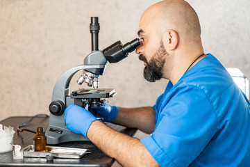 Male laboratory assistant examining biomaterial samples in a microscope.