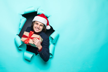 Surprised young man in santa hat holds Christmas gift through paper hole. Christmas sales. Black...