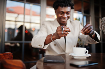 Stylish afro man in beige old school suit sitting on cafe with cup of coffee. Fashionable young African male in casual jacket on bare torso.