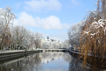 Isar river flows among the cold white landscape of the city of Munich in the snow, a park in...
