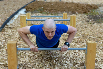 Athlete young man doing push-up exercise working out his upper body muscles outside in city park....
