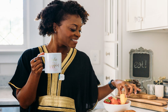 Woman eating fruit for breakfast as she holds coffee cup