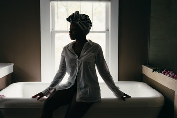 Woman relaxes by bathtub wearing head wrap