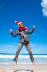 Excited barefoot businessman wearing Santa hat jumping for holiday joy on a tropical beach