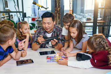 Young creative teacher explains for students the principle of quadcopter work.