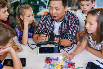 Young creative teacher explains for students the principle of quadcopter work.