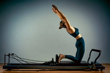 Young girl doing pilates exercises with a reformer bed. Beautiful slim fitness trainer on reformer...