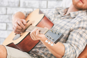 Handsome man playing guitar at home, closeup