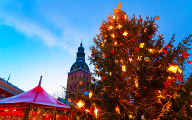 Fototapeta premium Night Cityscape with Christmas Market at Dome Cathedral square in Winter Riga, Latvia. Advent Fair Decoration and Stalls with Crafts Items on the Bazaar. Latvian street Xmas and holiday