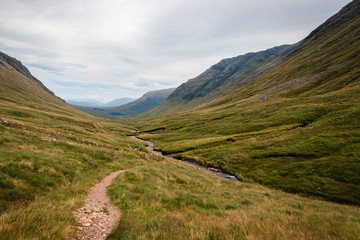 Panoramatic view on Scotland highland valley, during sunset with clouds, green yellow grass painting typical summer view with river in the middle