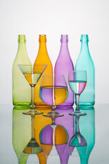 Coloured glass bottles with glasses with water coloured reflections. Reflected on a mirror on a white background