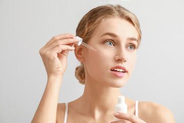 Naklejka premium Beautiful young woman with cosmetic product on light background