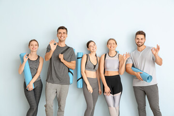 Fototapeta na wymiar Group of people with yoga mats showing OK near color wall