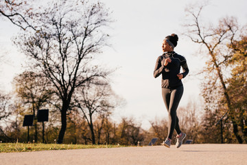 Full length of black female athlete running in autumn park.