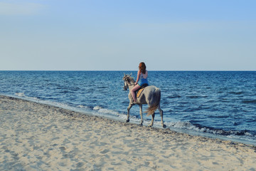 A woman rides a horse along the sea on the evening beach