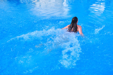 Girl swimming breaststroke in the pool, back view