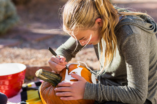 A teenage girl carving pumpkin outdoors at Halloween.