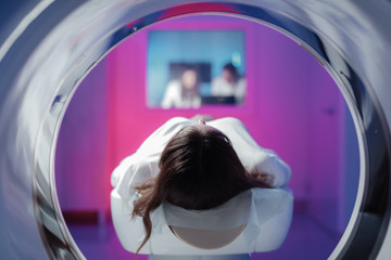 The girl patient is lying in the tomograph and waiting for a scan. Three doctors from the exam room...
