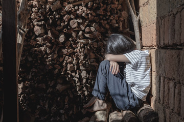 Homeless little girl in old dirty ragged clothes with depression sitting alone on firewood