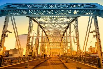 Sunset shine thru the bridge with unrecognised tourist walking over buildings sky background.