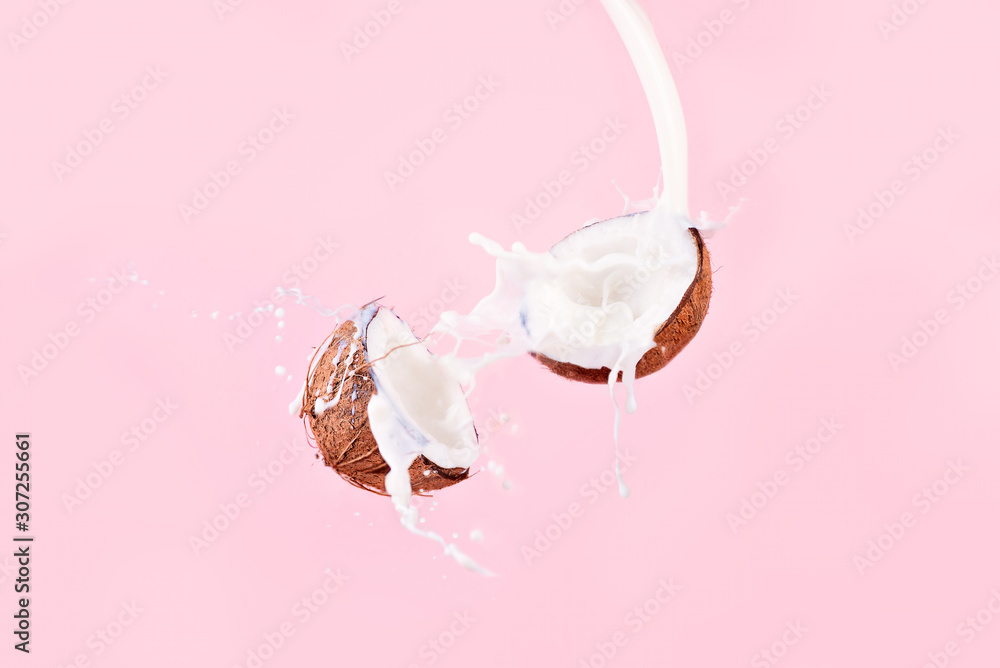 Wall mural coconut and spray of coconut milk over pink background, broken coconut levitation