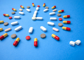 Group of different pills arranged in form of clock on blue background. Time in pharmacy. Time in medicine. 