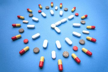 Group of different pills arranged in form of clock on blue background. Time in pharmacy. Time in...