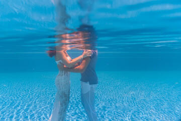 Beautiful romantic couple of bride and groom after wedding swimming gently under water and relax