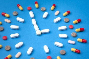 Group of different pills arranged in form of clock on blue background. Time in pharmacy. Time in medicine. 