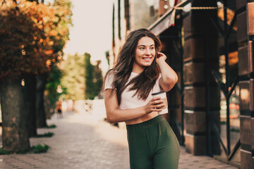 Smiling woman drink coffee walking on the city in summer day.