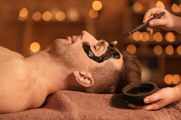 Cosmetologist applying mask onto man's face in spa salon