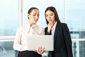 Beautiful businesswomen with laptop discussing issue in office