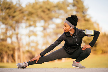Black athletic woman stretching her leg while working out in nature.