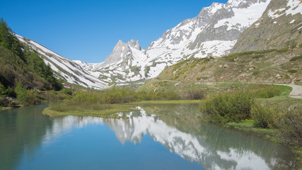 Naklejka na ściany i meble Mountains peaks mirroring in the lake showing symmetry. Mountains are full of snow and the water is calm. Val Veny, Italy