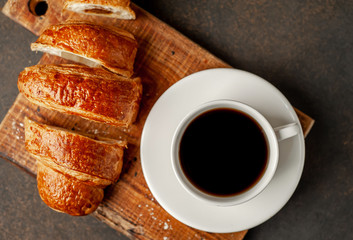 coffee and a large sliced ​​croissant on a stone table with copy space for your text, early breakfast concept