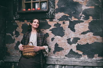 Young brunette woman in retro clothes sits under the window of an old house, copy space for text. Halloween gothic vintage costume