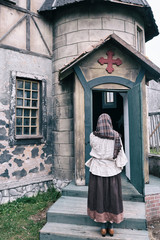 Fototapeta na wymiar A woman stands praying at the door of an old catholic church
