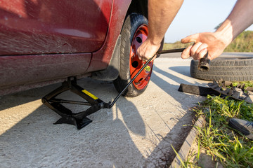man lifts the car with a jack to install a spare tire