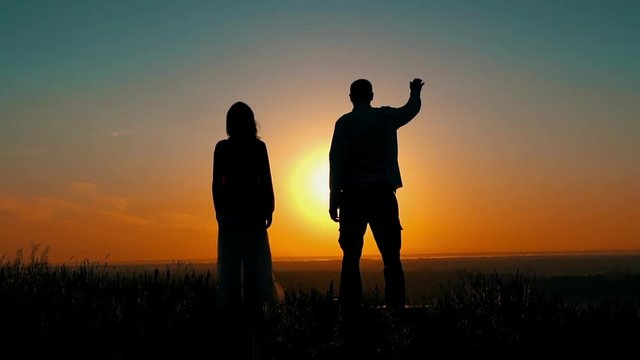 silhouette of man and woman waving hands standing on the hill at sunrise enjoy beautiful landscape orange sky slow motion