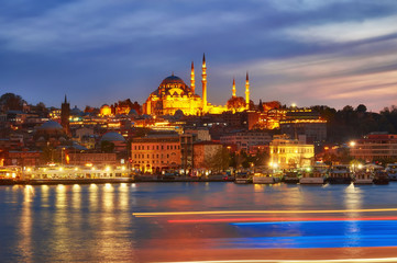 Night view at Yeni Cami Mosque worship place from Galata bridge reflected in water of Golden Horn of Bosporus.