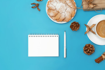 Notebook with isolated white page, coffee cup, ginger cookies and craft gift box on cyan blue background. Holiday season concept. Copy space. Flat lay style.