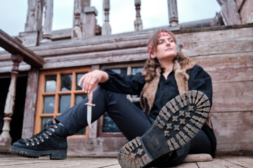 Pirate girl sitting on wooden floor with Dirk hand, selective focus on shoe